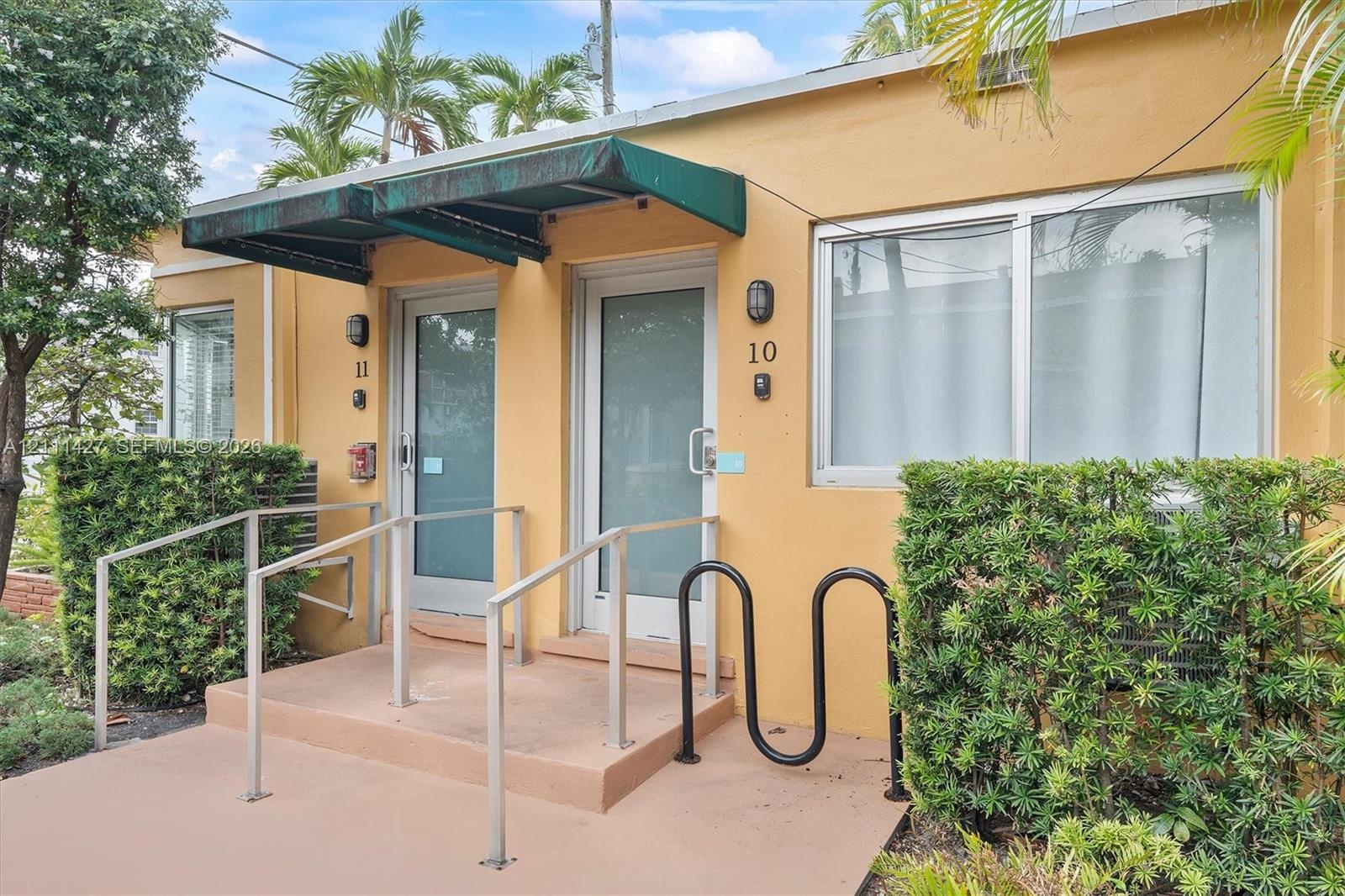 Exterior facade featuring stucco siding, metal-frame glass entry doors, green metal awnings, and metal handrails