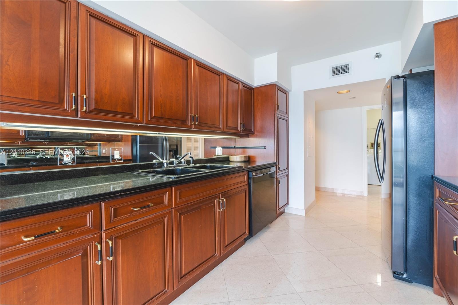 Kitchen featuring raised-panel wood cabinetry, black countertops, mirrored backsplash, under-cabinet lighting, and black appliances