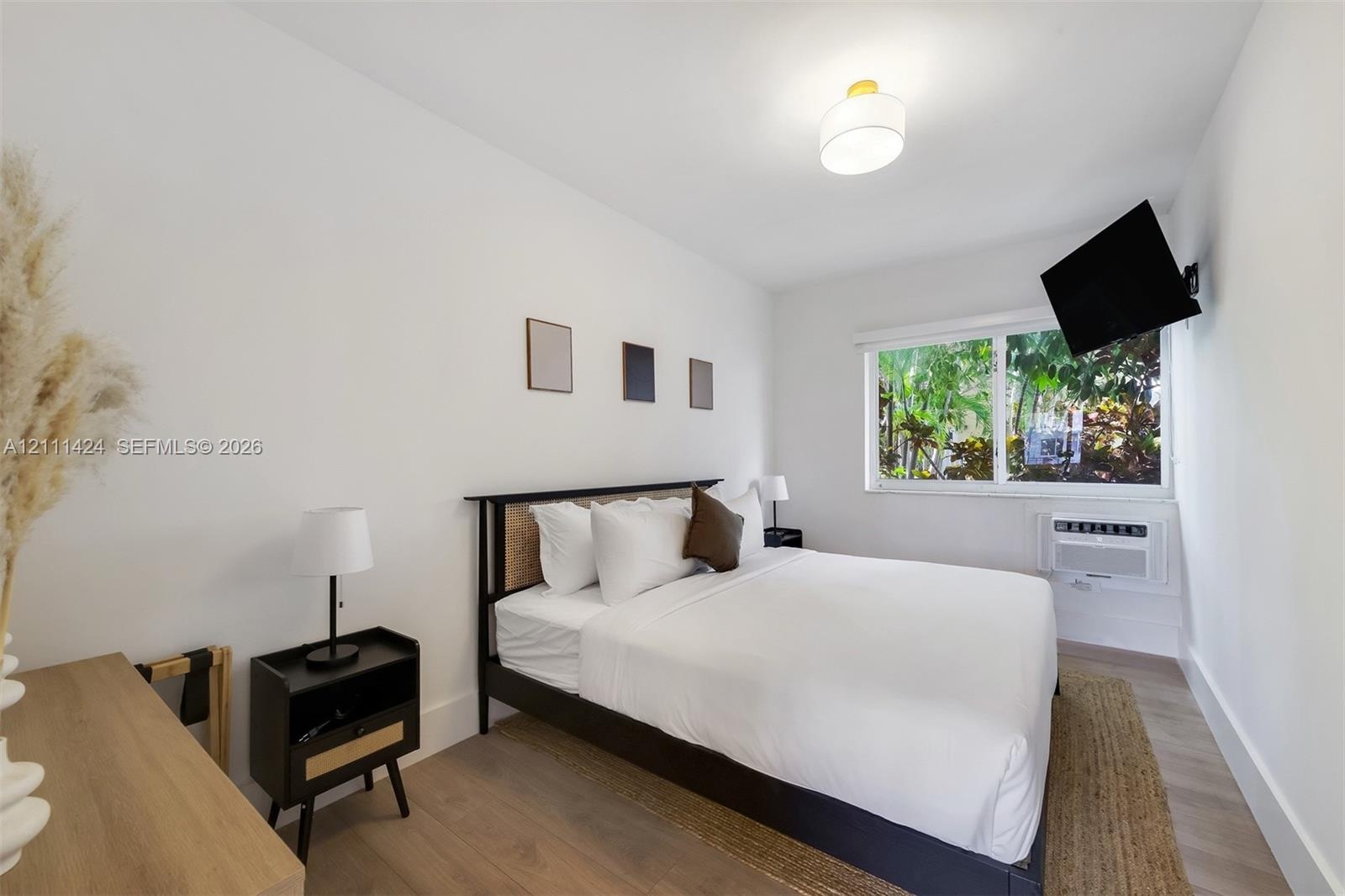 Bright room featuring wood-finish flooring, a large window, a wall-mounted cooling unit, and a flush-mount drum ceiling light fixture