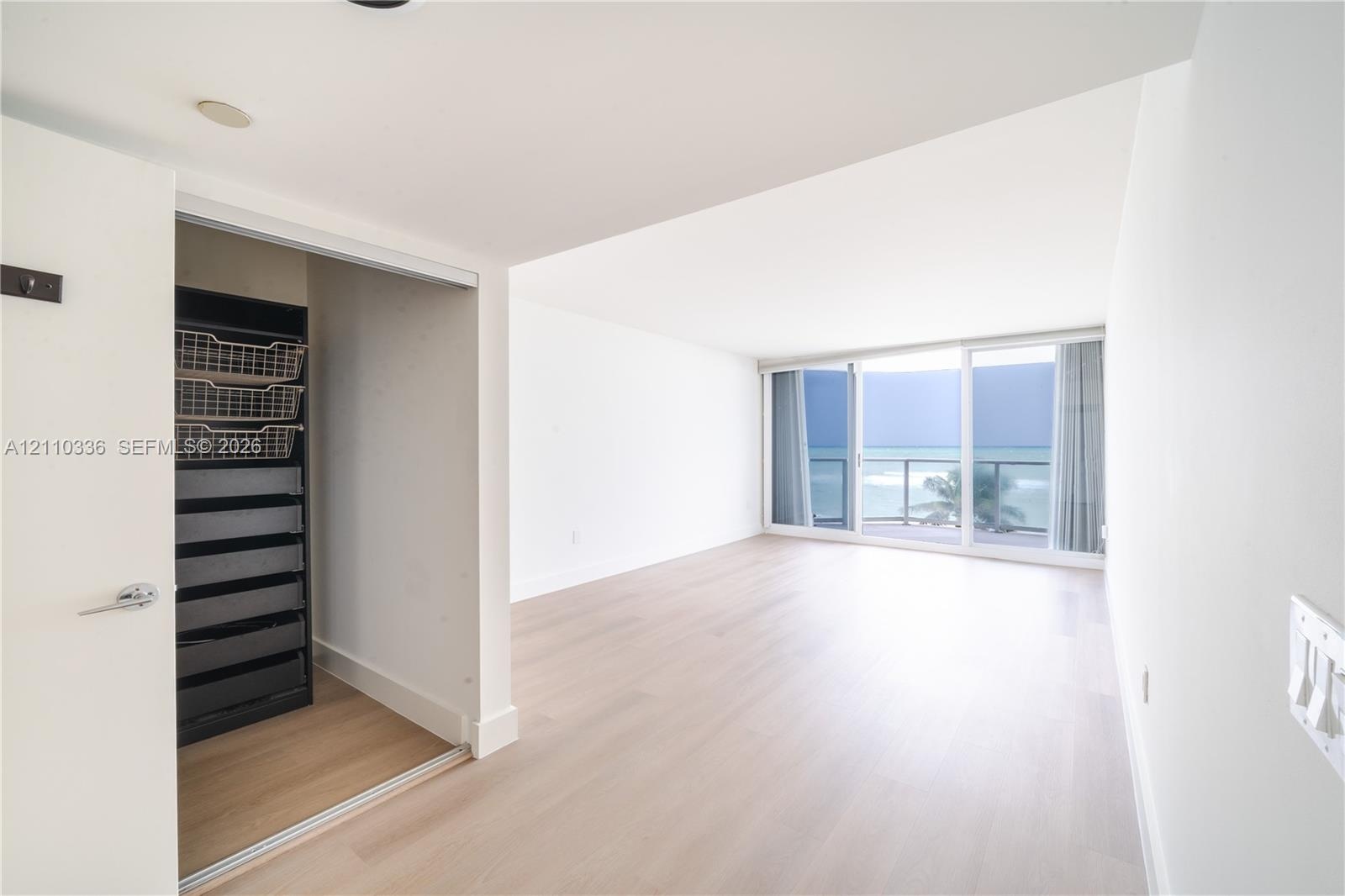 Living area featuring light wood-finish flooring, floor-to-ceiling sliding glass doors, built-in closet organization system, and ocean horizon backdro