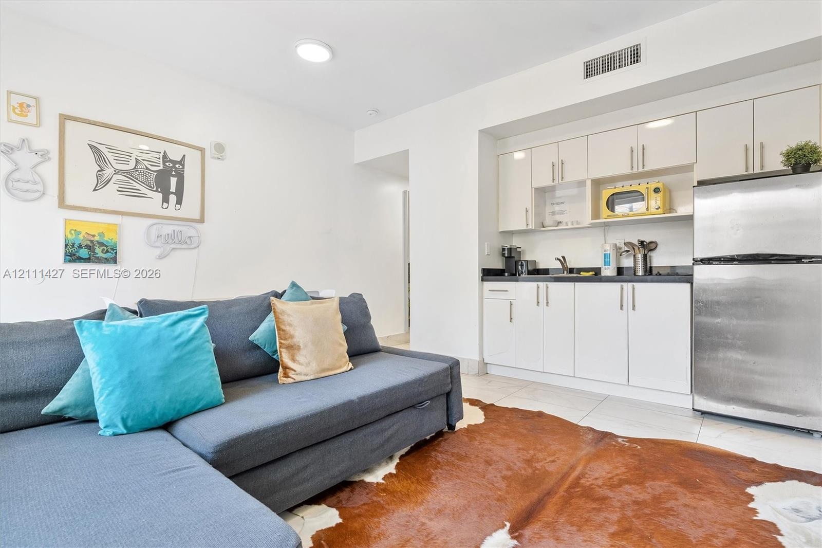 Kitchenette featuring white cabinetry, black countertops, and stainless steel refrigerator
