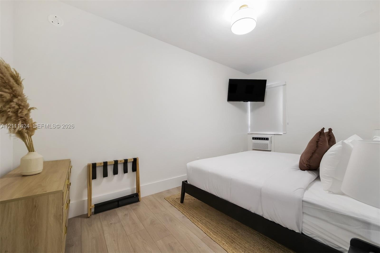 Neutral-toned room featuring wood-finish flooring, a wall-mounted climate control unit, and a flush-mount ceiling light fixture