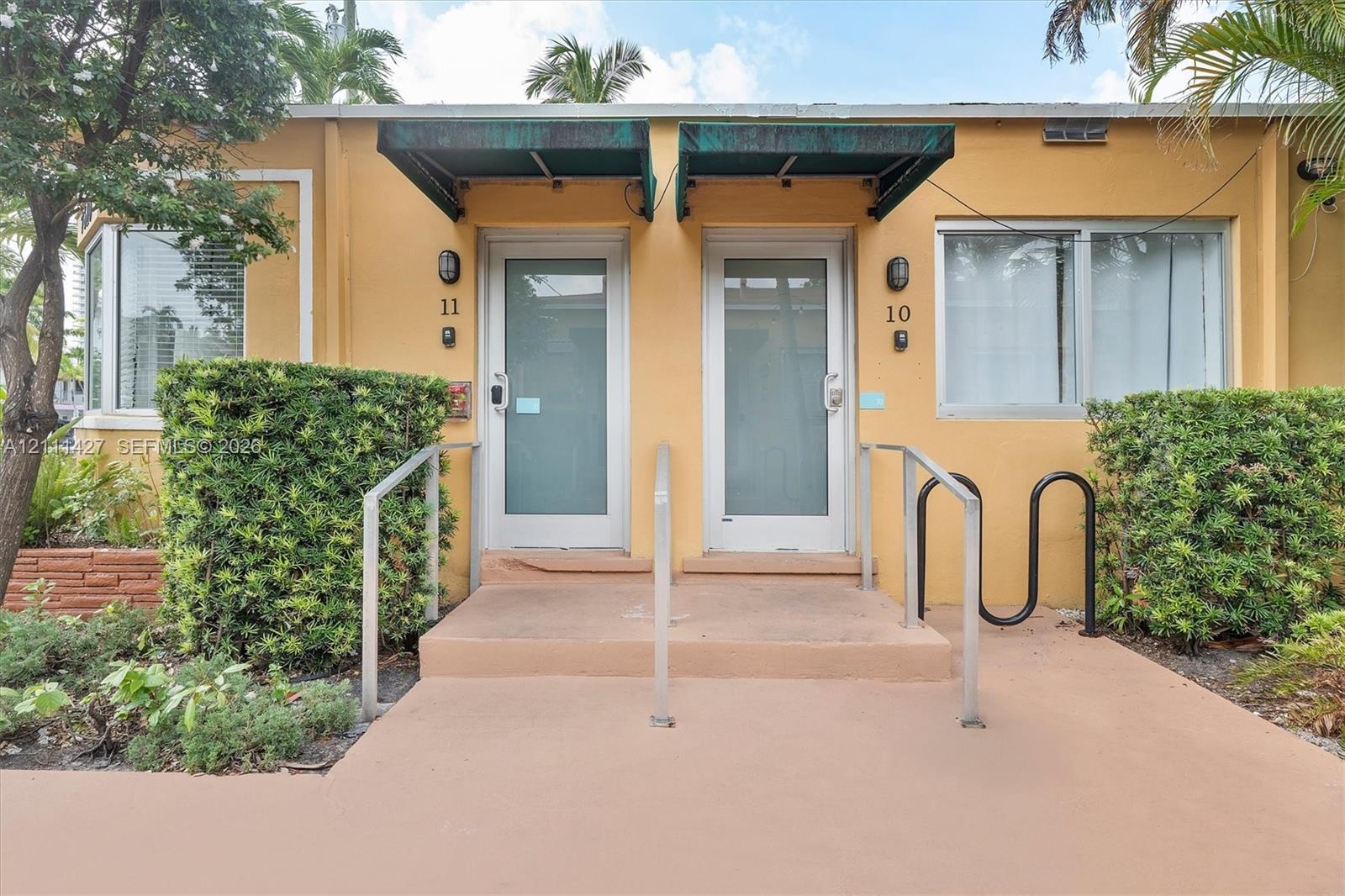 Exterior facade featuring two glass-paneled entry doors, metal awnings, and concrete steps with metal handrails