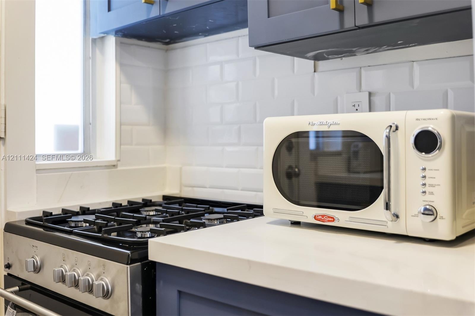 Kitchen featuring dark blue cabinetry with brushed gold hardware, quartz countertops, white subway tile backsplash, and a stainless steel gas range