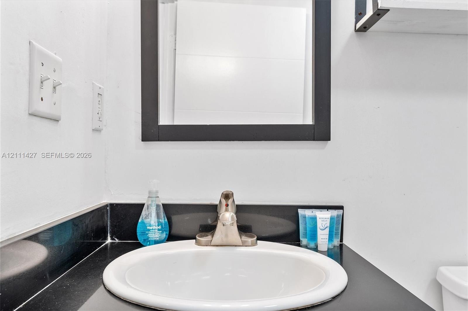 Bathroom vanity featuring a dark solid-surface countertop, an integrated white oval sink, and a high-arch metal faucet, accented by a black-framed wal