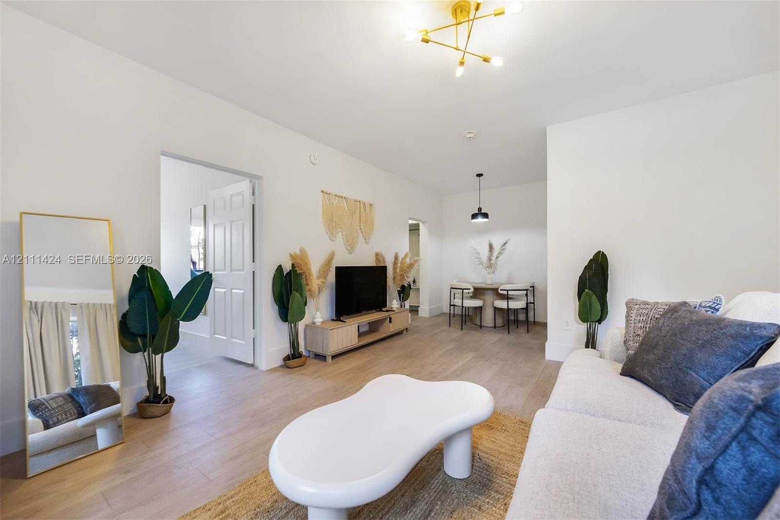 Open-concept interior featuring light wood-finish flooring, a multi-arm brass finish ceiling fixture, and a neutral color palette