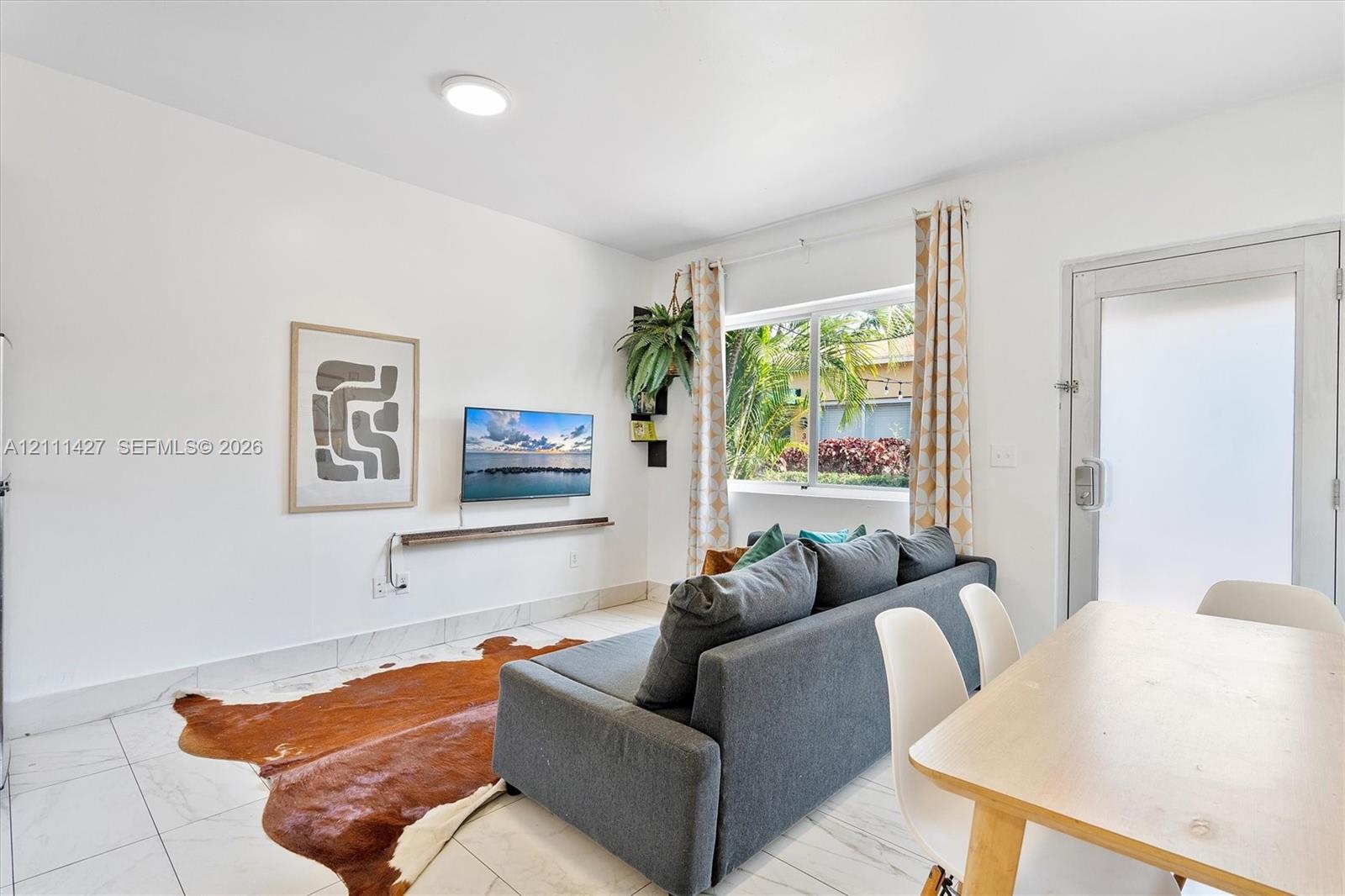 Bright living area featuring large-format stone-finish tile flooring, a wall-mounted display shelf, and a sliding glass exterior door