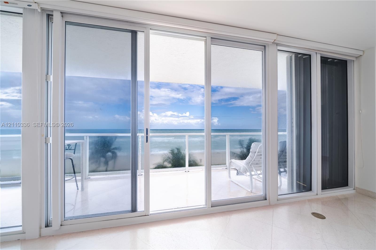 Floor-to-ceiling sliding glass panels, balcony with glass railing, stone flooring, and expansive ocean scenery