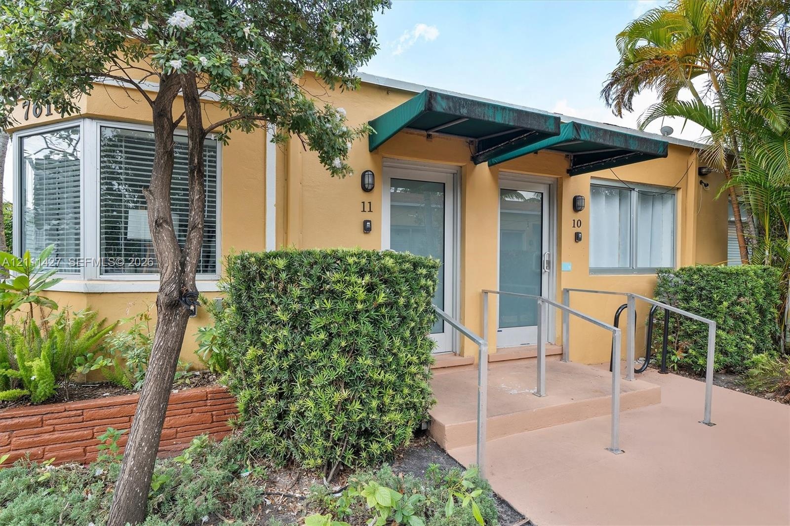 Stucco exterior featuring dual entryways with metal awnings, bay window, and concrete step access with metal handrails