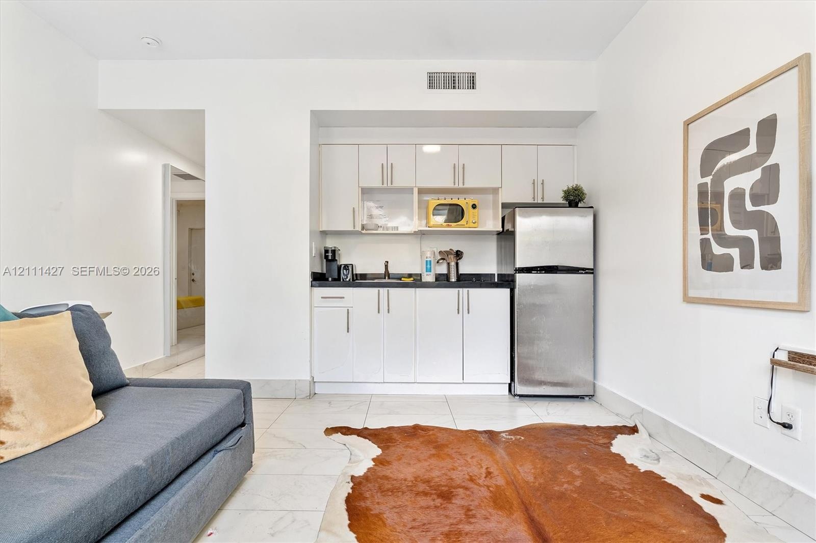 Kitchenette featuring white cabinetry, dark stone countertops, stainless steel refrigerator, and large-format tile flooring