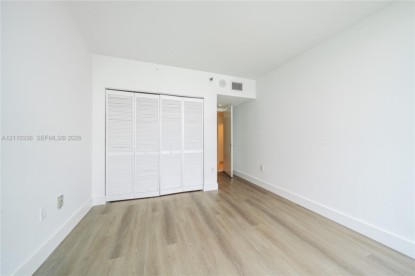 Room featuring wood-finish flooring, white walls, and a closet with bifold louvered doors