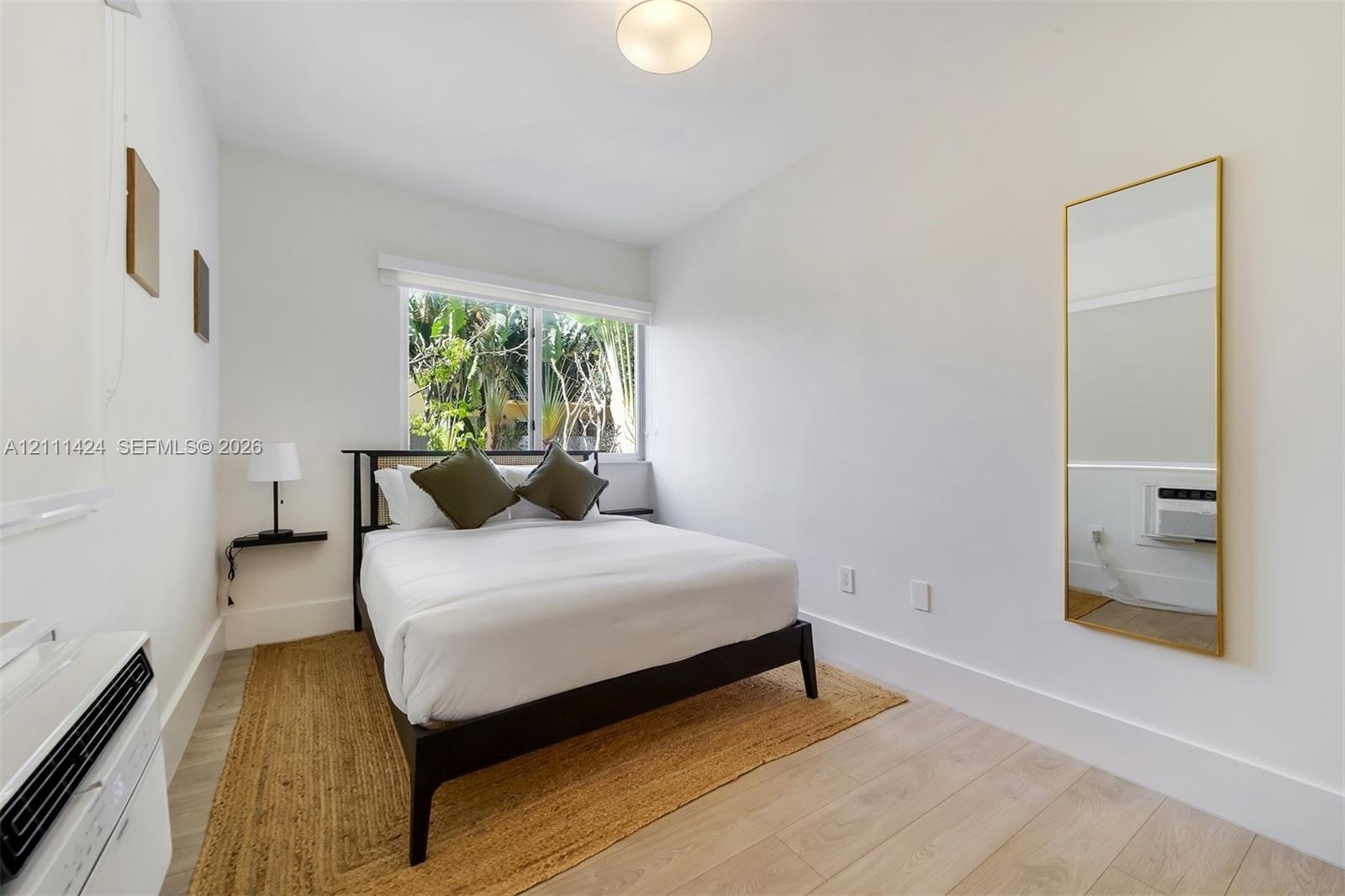 Neutral-toned space featuring light-toned wood-finish flooring, a large window with white horizontal blinds, and a mounted wall-air conditioning unit