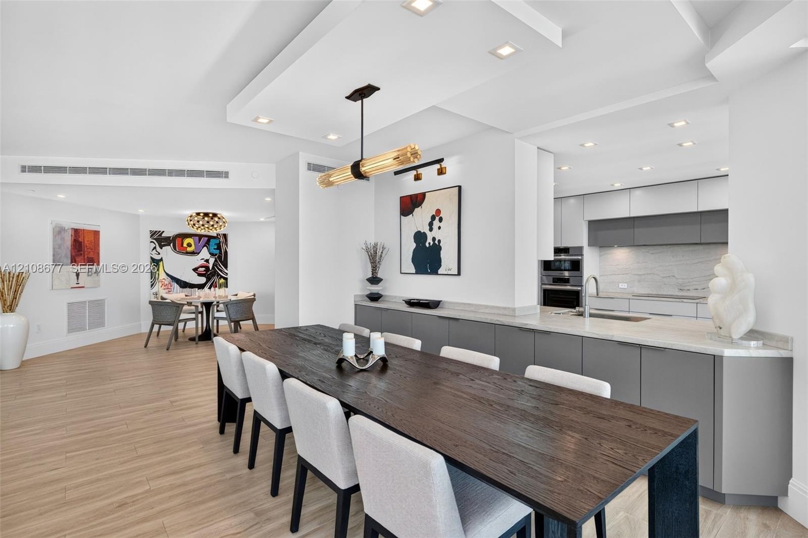 Open-concept dining space space featuring wood look plank porcelain flooring, a coffered ceiling with recessed lighting, minimalist flat-panel cabinet