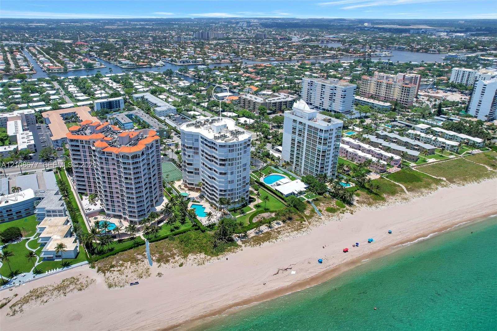 Aerial perspective of coastal high-rise condominiums featuring direct beachfront access, expansive sandy shoreline, outdoor swimming pools, and manicu