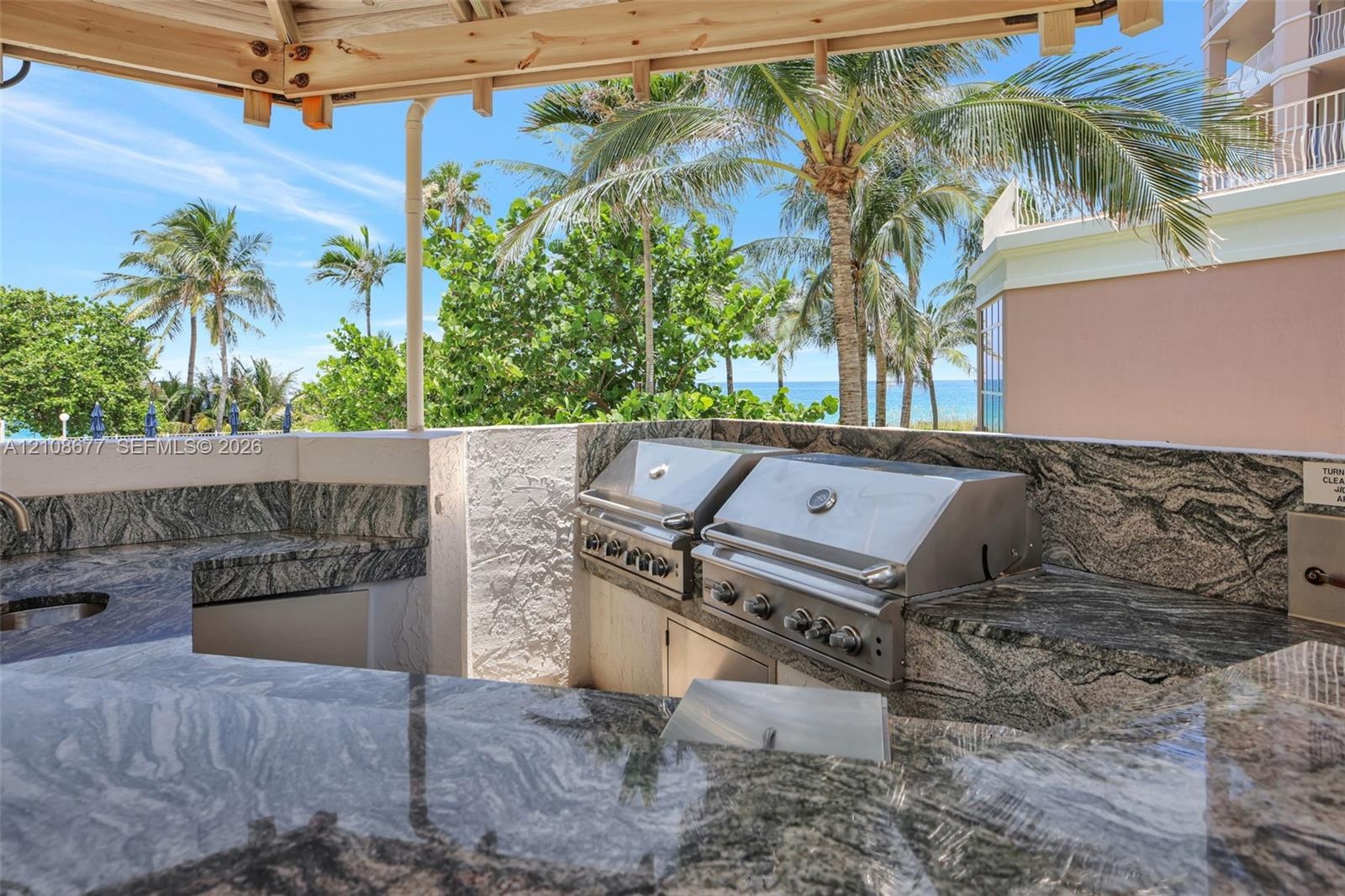 Outdoor BBQ kitchen featuring stone countertops, dual stainless steel built-in grills, a covered structure, and water views