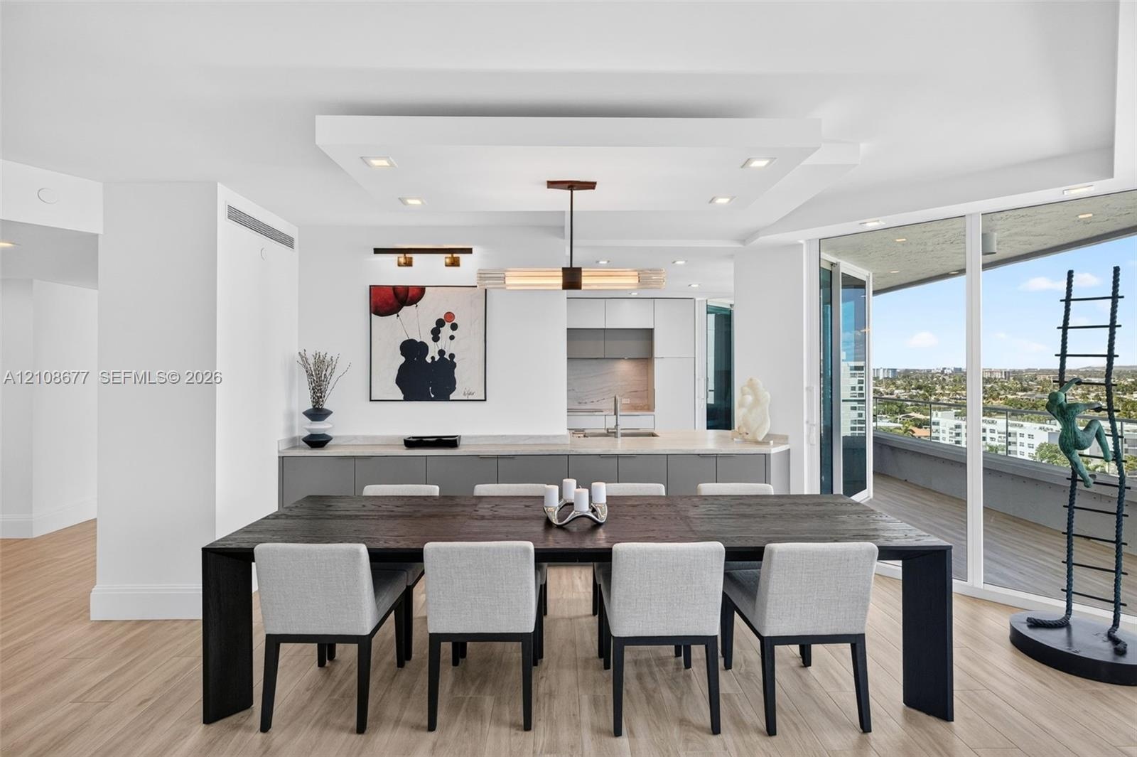 Open-concept kitchen featuring flat-panel cabinetry, light-toned stone counters, wood look plank porcelain flooring, tray ceiling with recessed lighti
