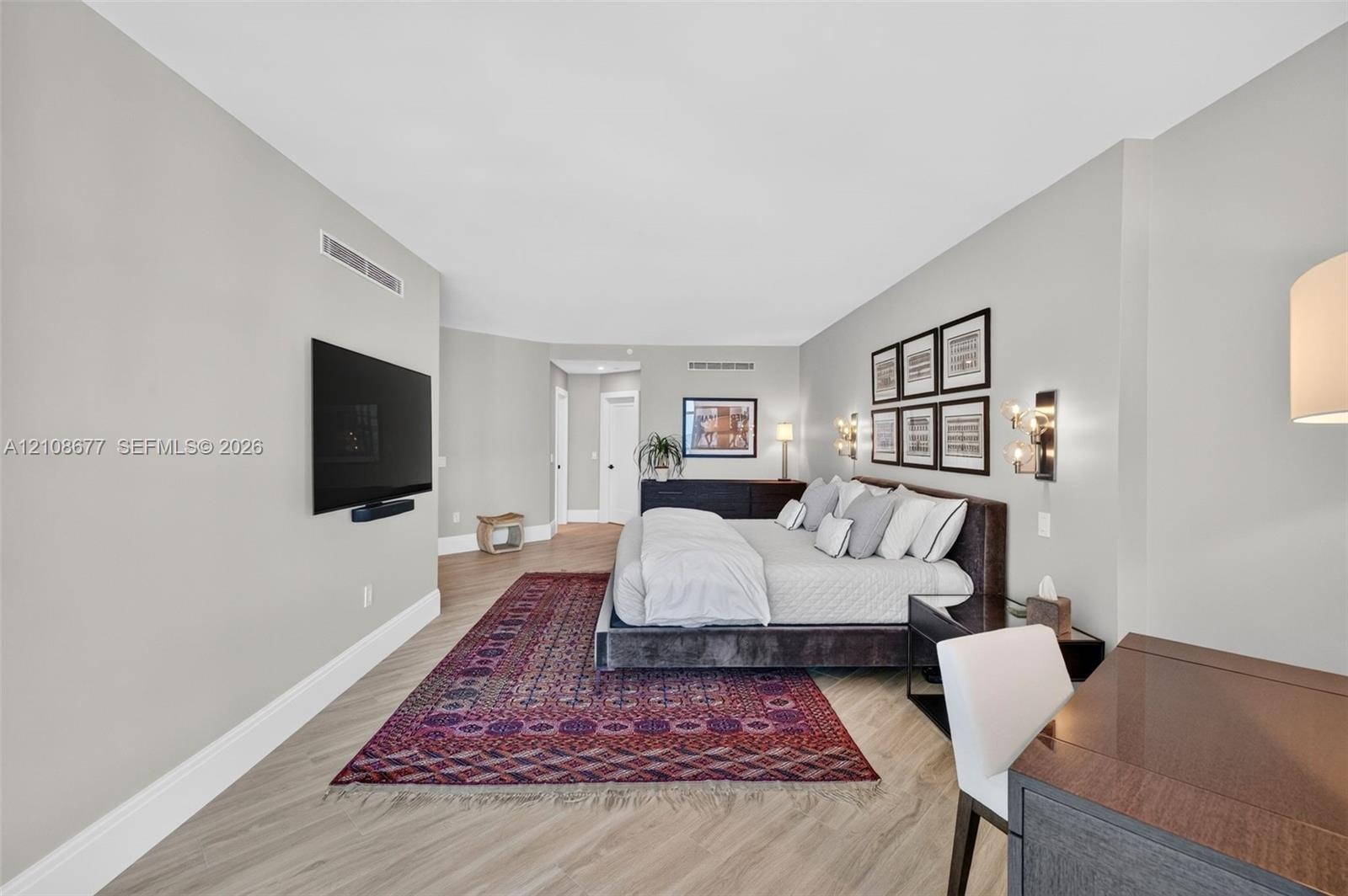 Spacious room featuring wood look plank porcelain flooring, neutral wall tones, and wall-mounted light fixtures. View toard primary bathroom and large