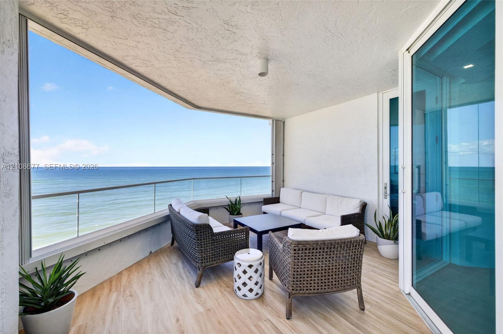Covered balcony featuring the same wood look plank porcelain flooring as interior, a frameless glass railing, and expansive ocean scenery. Additional 