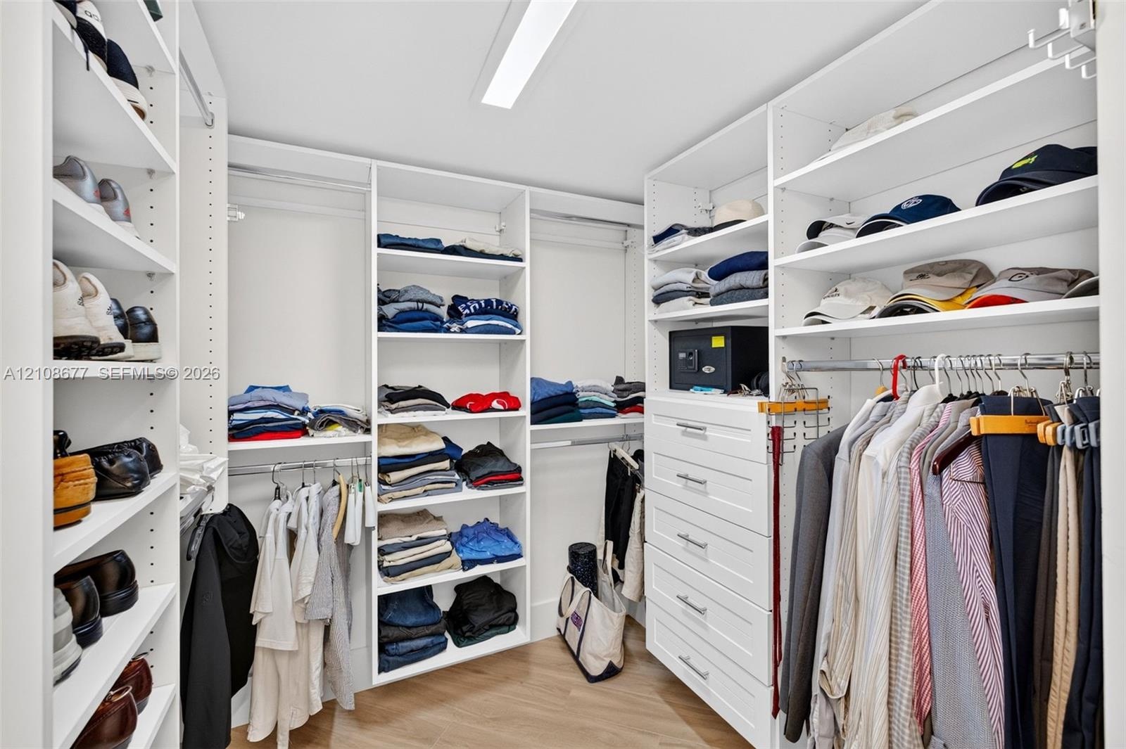 View toward shorter side of the custom walk-in closet featuring floor-to-ceiling white shelving, integrated clothing rods, stacked drawer storage, and