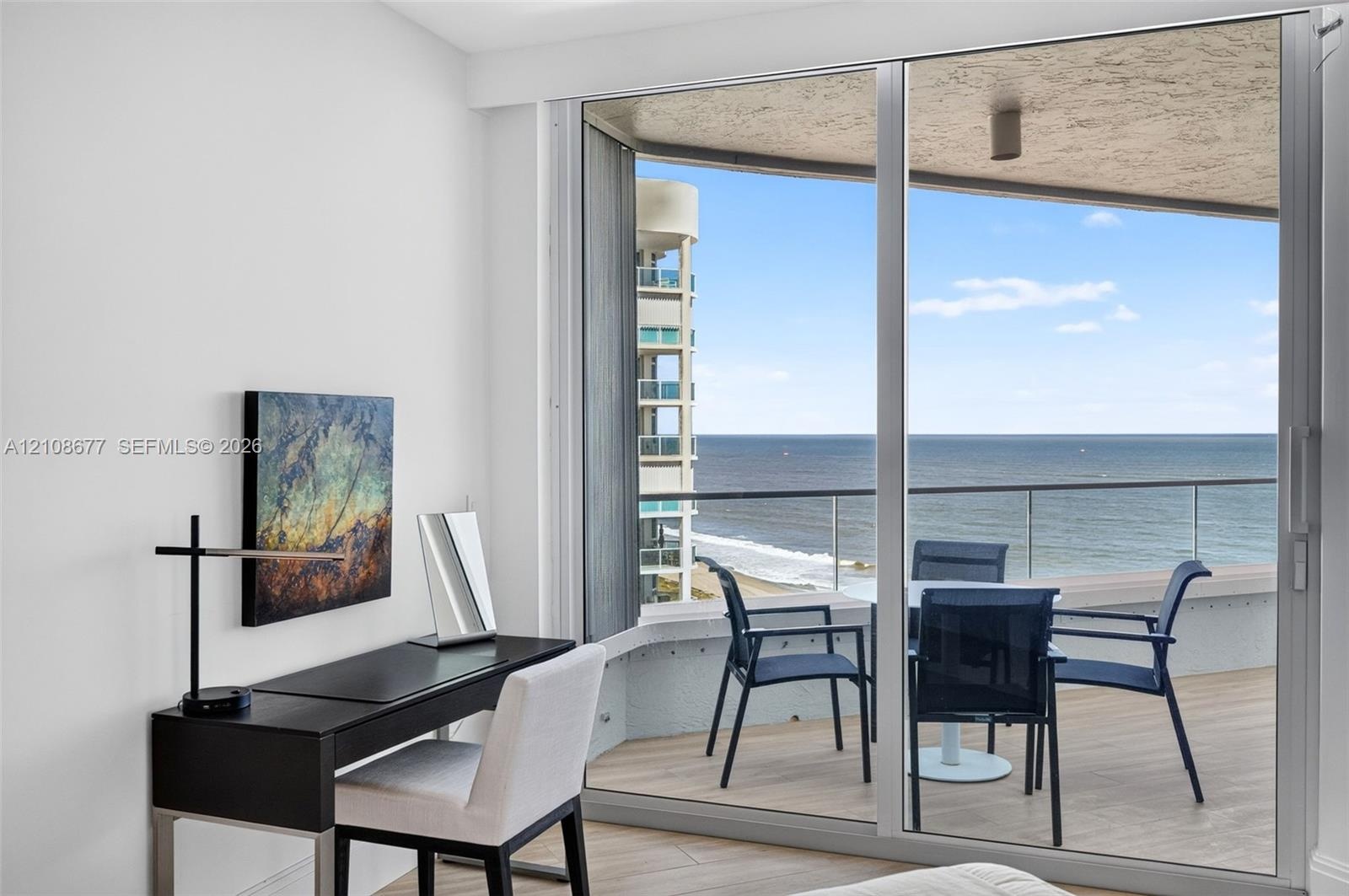 Full-height sliding glass doors opening to a private balcony with glass railing, wood look plank porcelain flooring, and ocean scenery. Double layered
