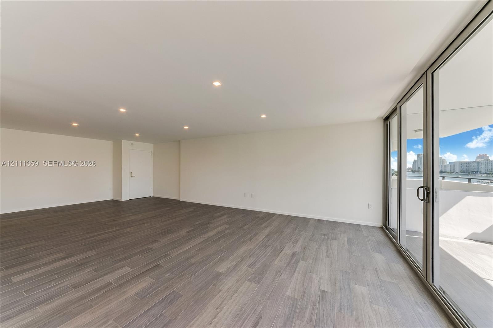 Open-concept living space featuring wood-finish flooring, recessed ceiling lighting, and floor-to-ceiling glass sliding doors leading to an outdoor ba