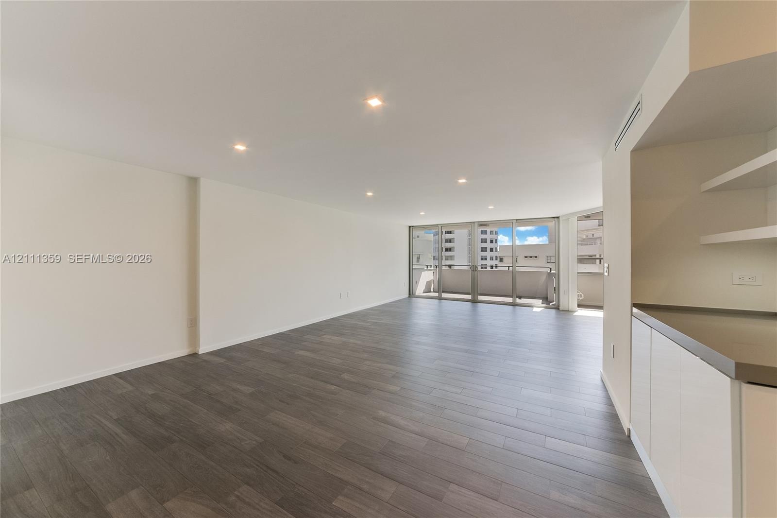 Open-concept interior featuring wood-finish flooring, recessed lighting, floor-to-ceiling glass sliding doors, private balcony, and built-in cabinetry