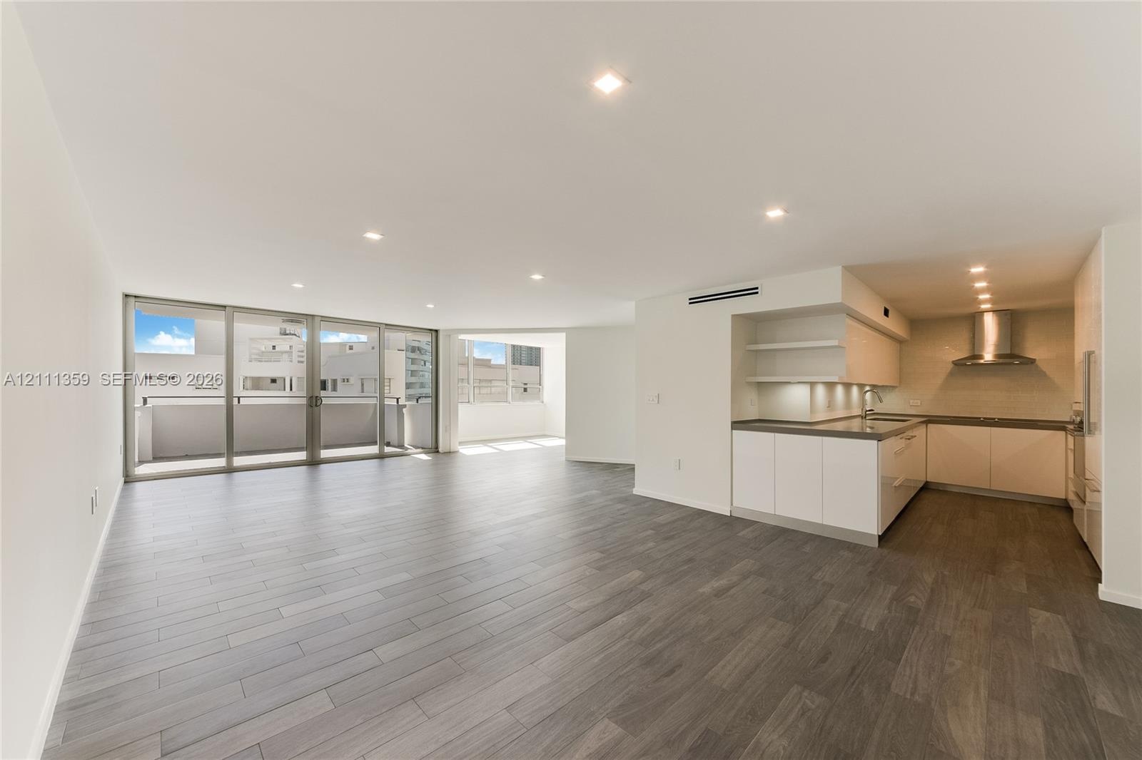 Open floor plan featuring wood-finish flooring, recessed lighting, floor-to-ceiling glass doors, and a kitchen equipped with cabinetry, stone-surface 