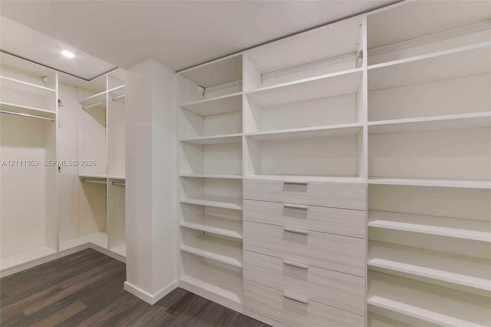 Walk-in closet featuring extensive built-in shelving, integrated wood-finish cabinetry, a bank of five drawers with metallic hardware, and dark wood-f
