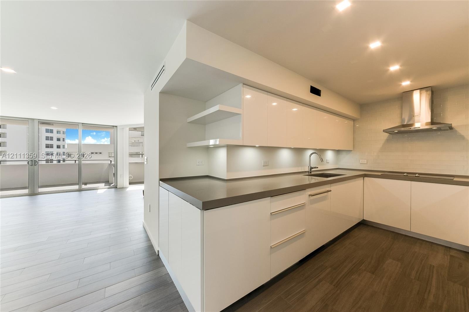 Modern kitchen featuring high-gloss white cabinetry, solid-surface countertops, stainless steel range hood, recessed lighting, and wood-finish floorin