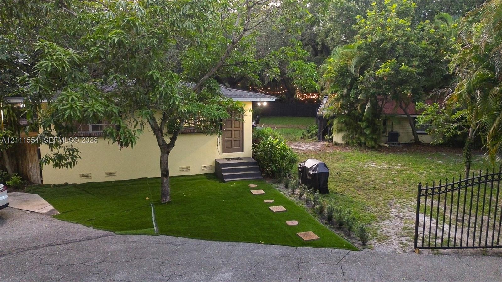 Stucco exterior dwelling featuring a multi-panel wood door, concrete paver pathway, artificial turf lawn, and ornamental metal fencing