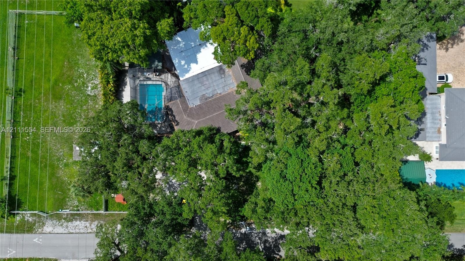 Aerial perspective featuring an expansive lot, mature tree canopy, fenced perimeter, and an in-ground pool with a screen enclosure