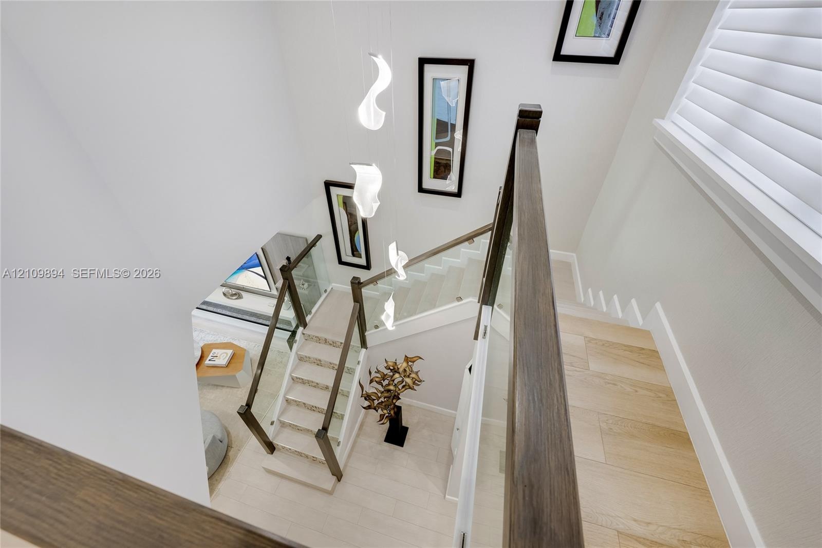 Staircase featuring glass panel railings, wood-finish handrails, multi-tiered sculptural pendant lighting, and light-toned flooring