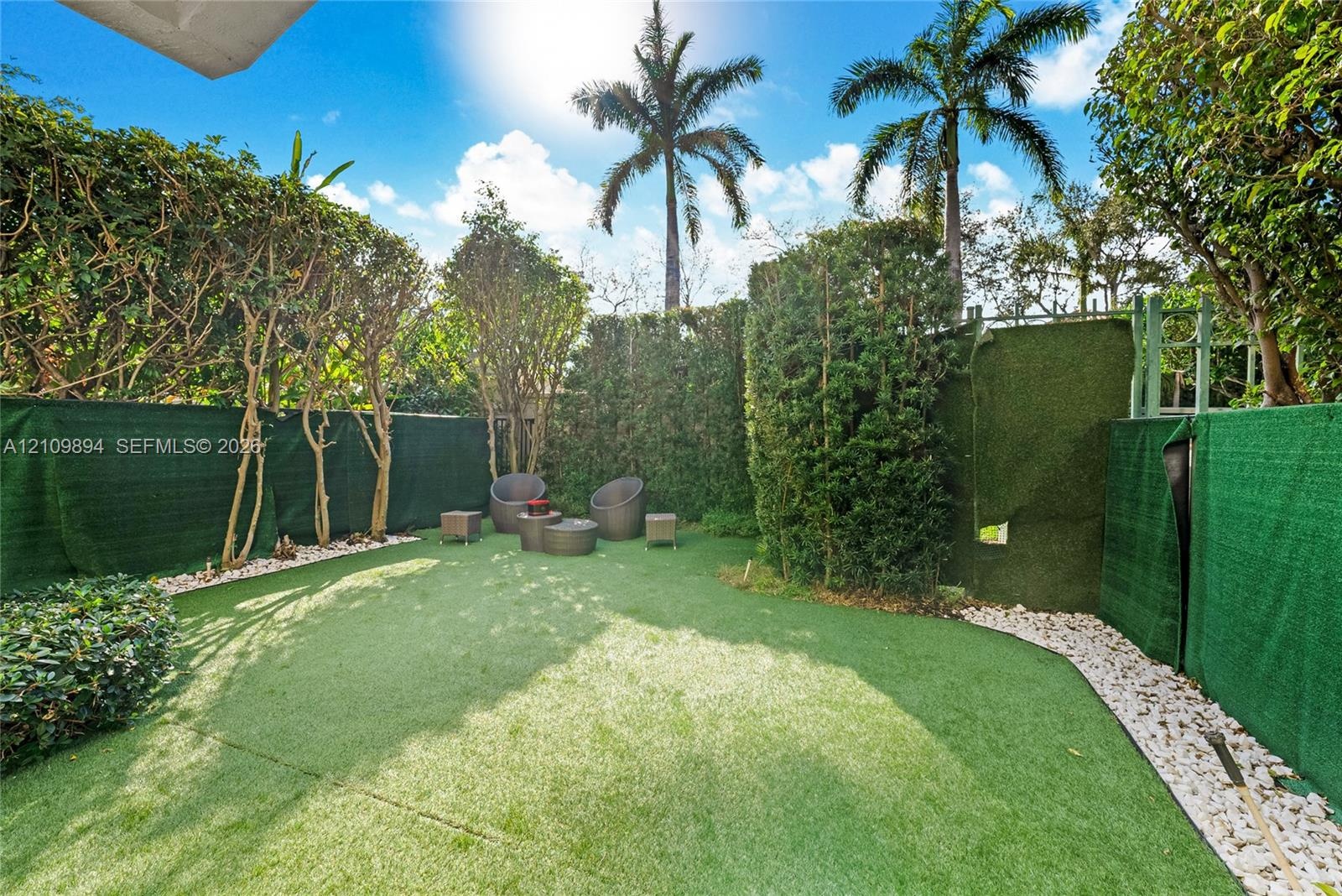 Private outdoor area featuring synthetic turf, perimeter privacy screening, mature landscape hedging, and decorative stone borders