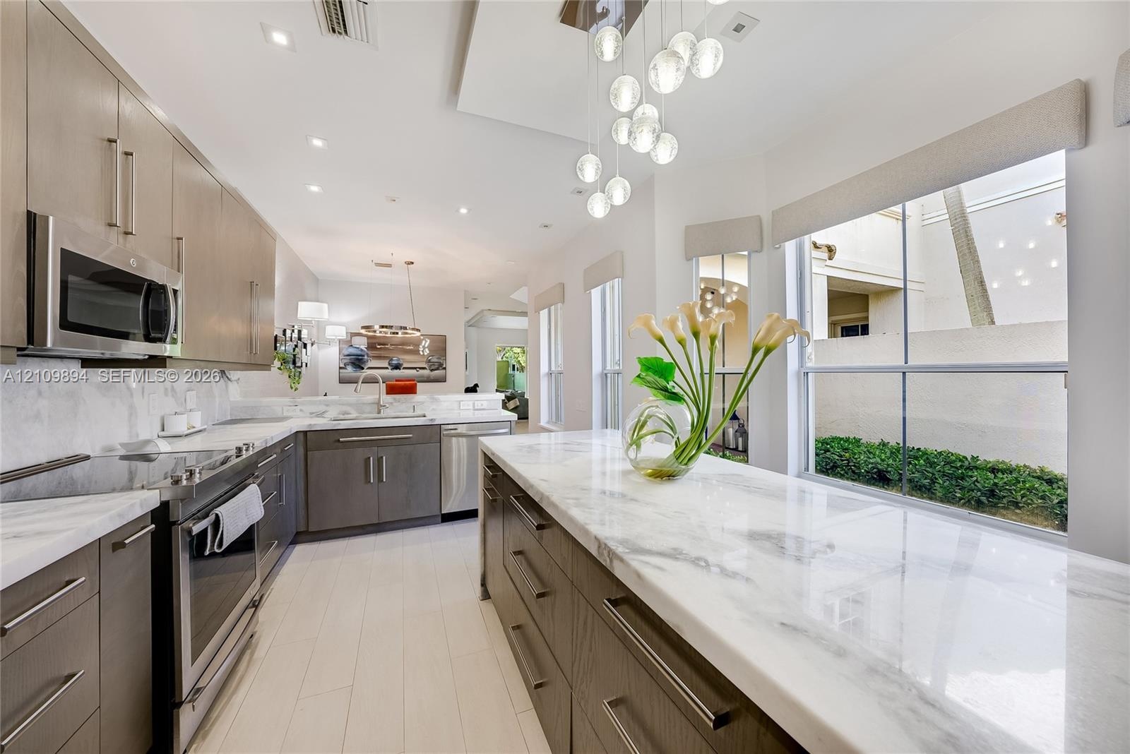 Kitchen featuring wood-finish cabinetry, stone countertops, stainless steel appliances, recessed ceiling lighting, and a multi-globe pendant light fix