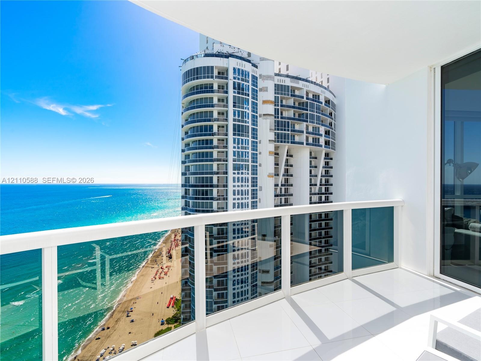 Private balcony with glass and metal railings, large-format tile flooring, and direct oceanfront exposure