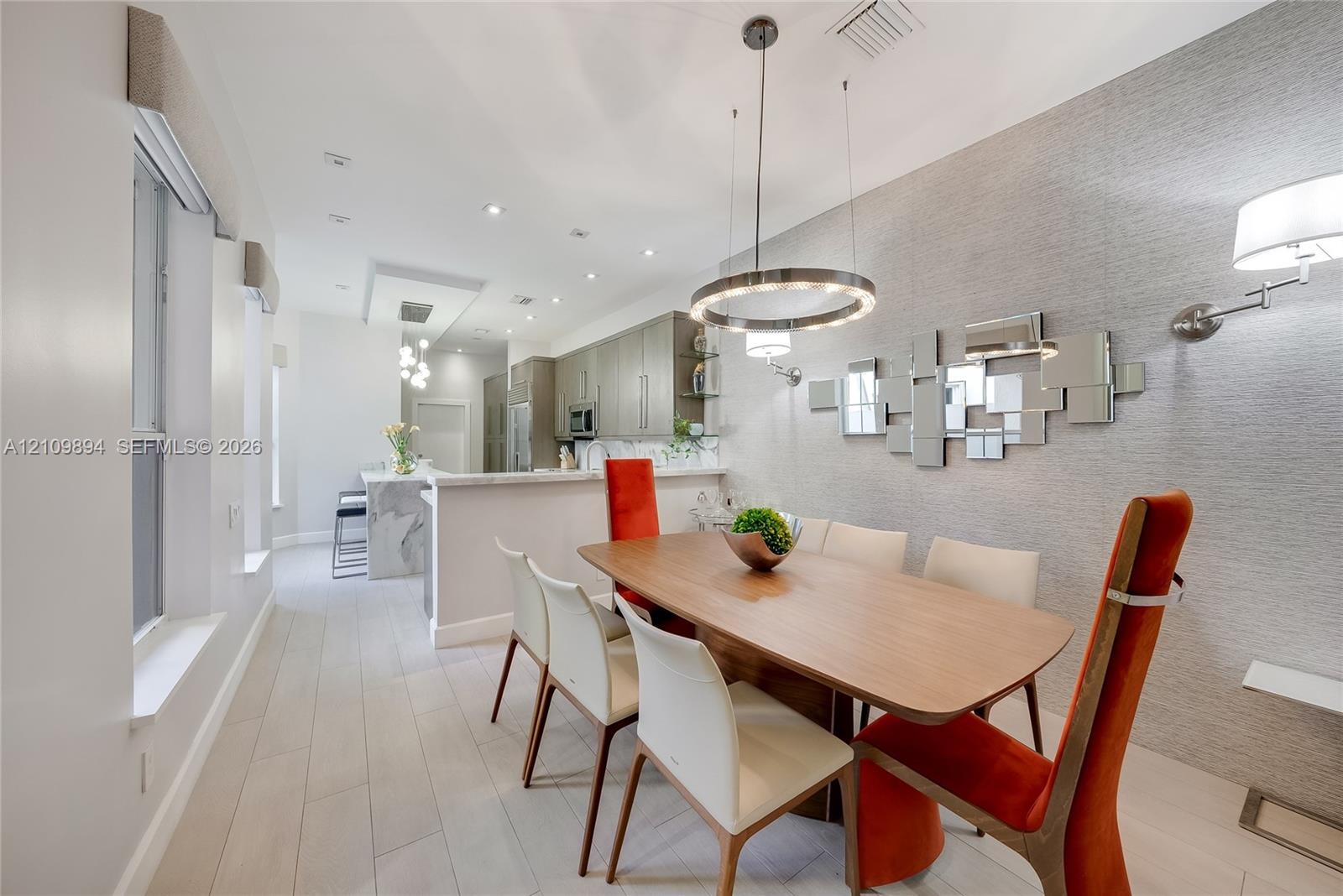 Light-toned wood-finish flooring, circular LED chandelier, textured wall covering, recessed ceiling lighting, and quartz-topped island with stone-fini