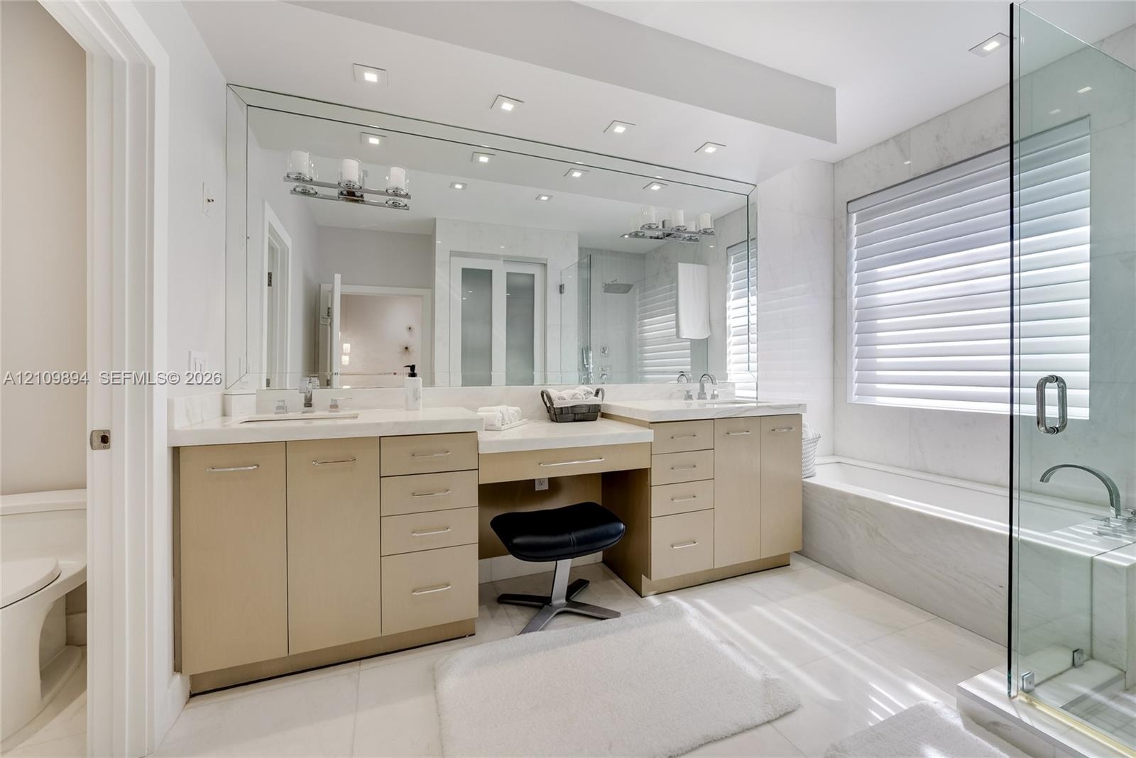 Double vanity featuring cabinetry with satin-finish hardware, integrated quartz countertops, an inset makeup station, full-width wall mirror, and a gl