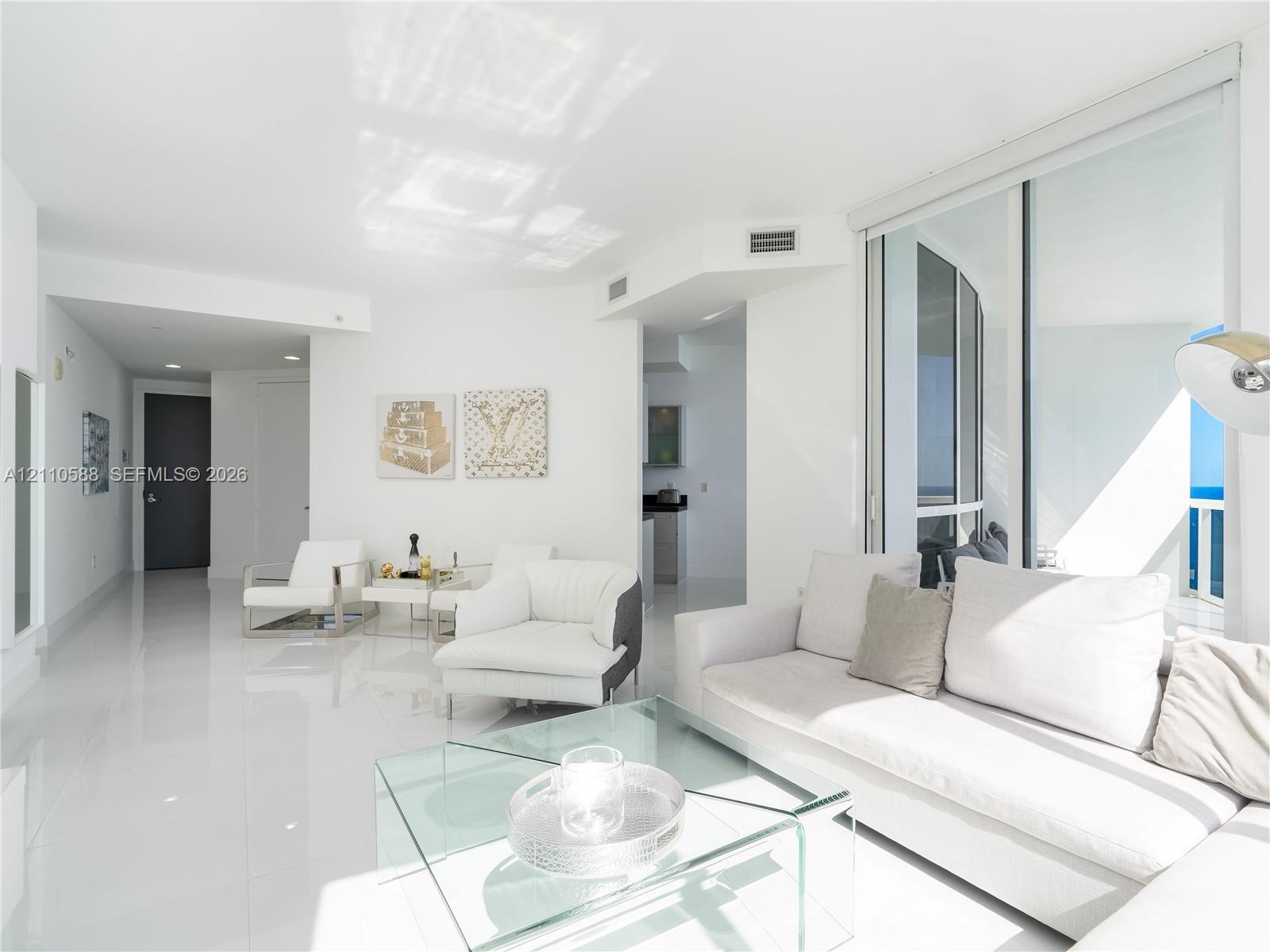 Open-concept living space with polished tile flooring, recessed ceiling lighting, and floor-to-ceiling glass sliding doors opening to an exterior balc