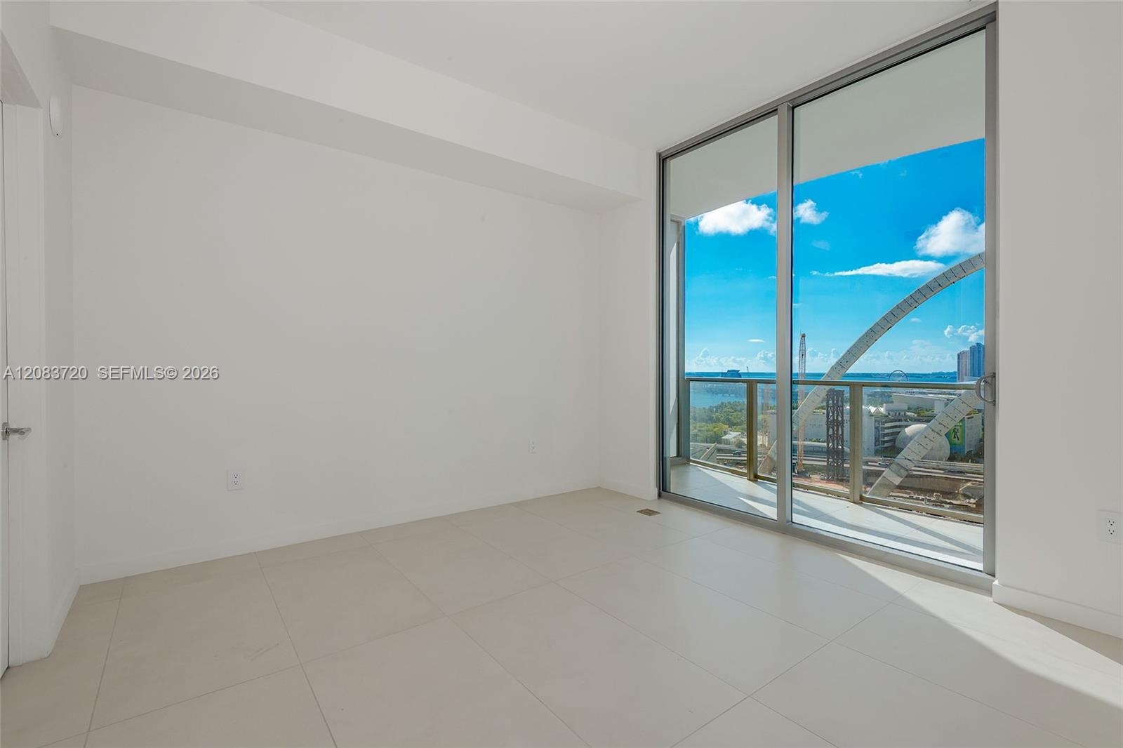 Floor-to-ceiling glass sliding doors, large-format tile flooring, and a private balcony featuring a metal railing