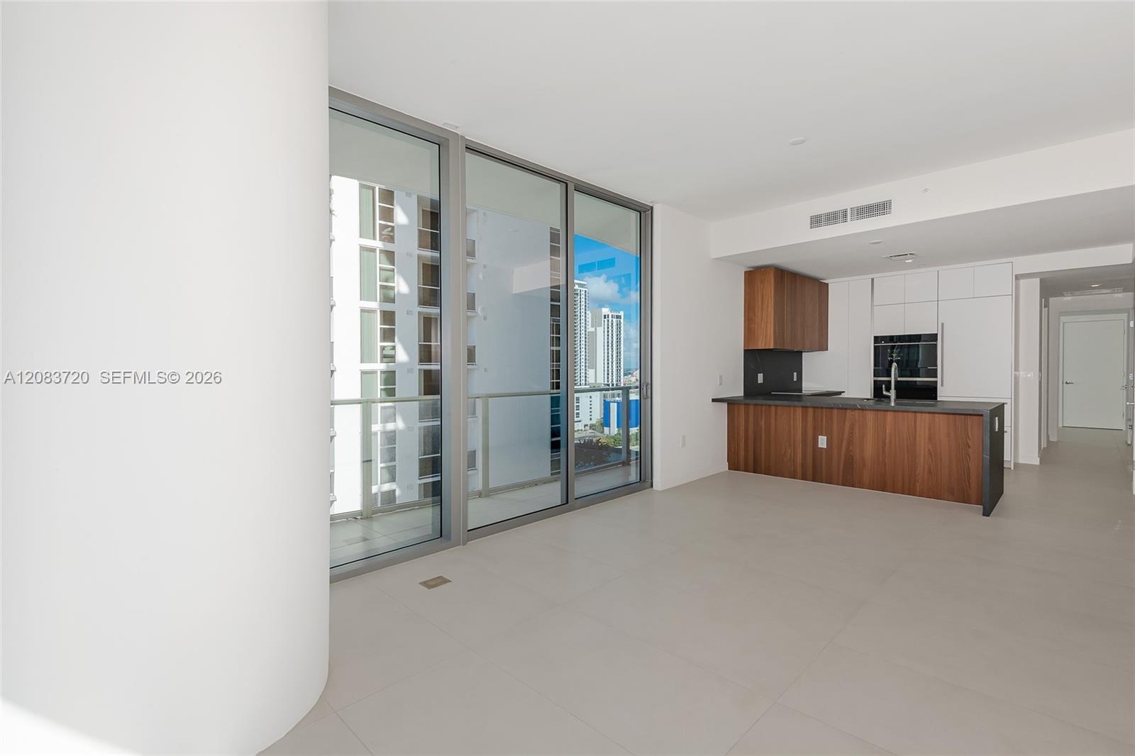 Floor-to-ceiling sliding glass doors, large-format tile flooring, kitchen featuring wood-finish cabinetry, white flat-panel upper cabinets, and dark s