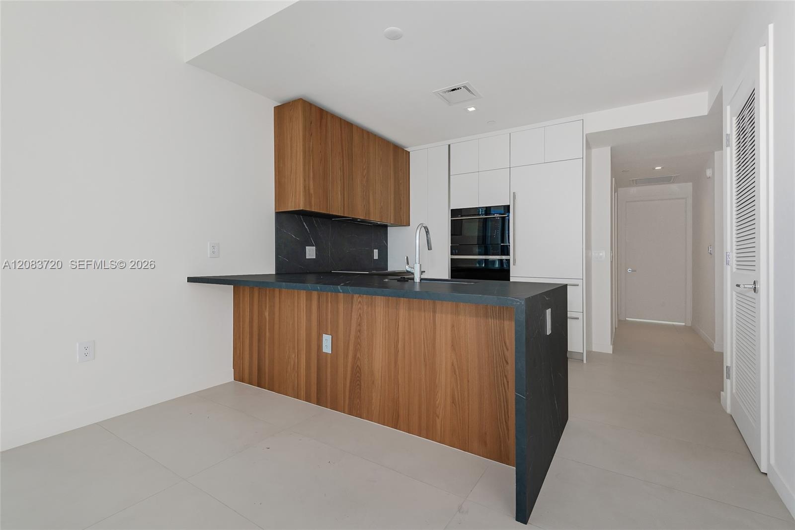 Kitchen featuring wood-finish cabinetry, dark stone-style countertops with a waterfall edge, matching full-height backsplash, stainless steel faucet, 