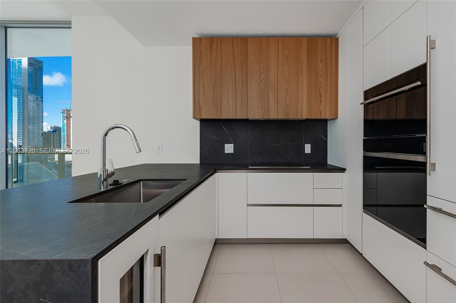 Kitchen featuring dual-toned flat-panel cabinetry, dark stone countertops, an integrated stainless steel sink with a high-arch faucet, and built-in wa