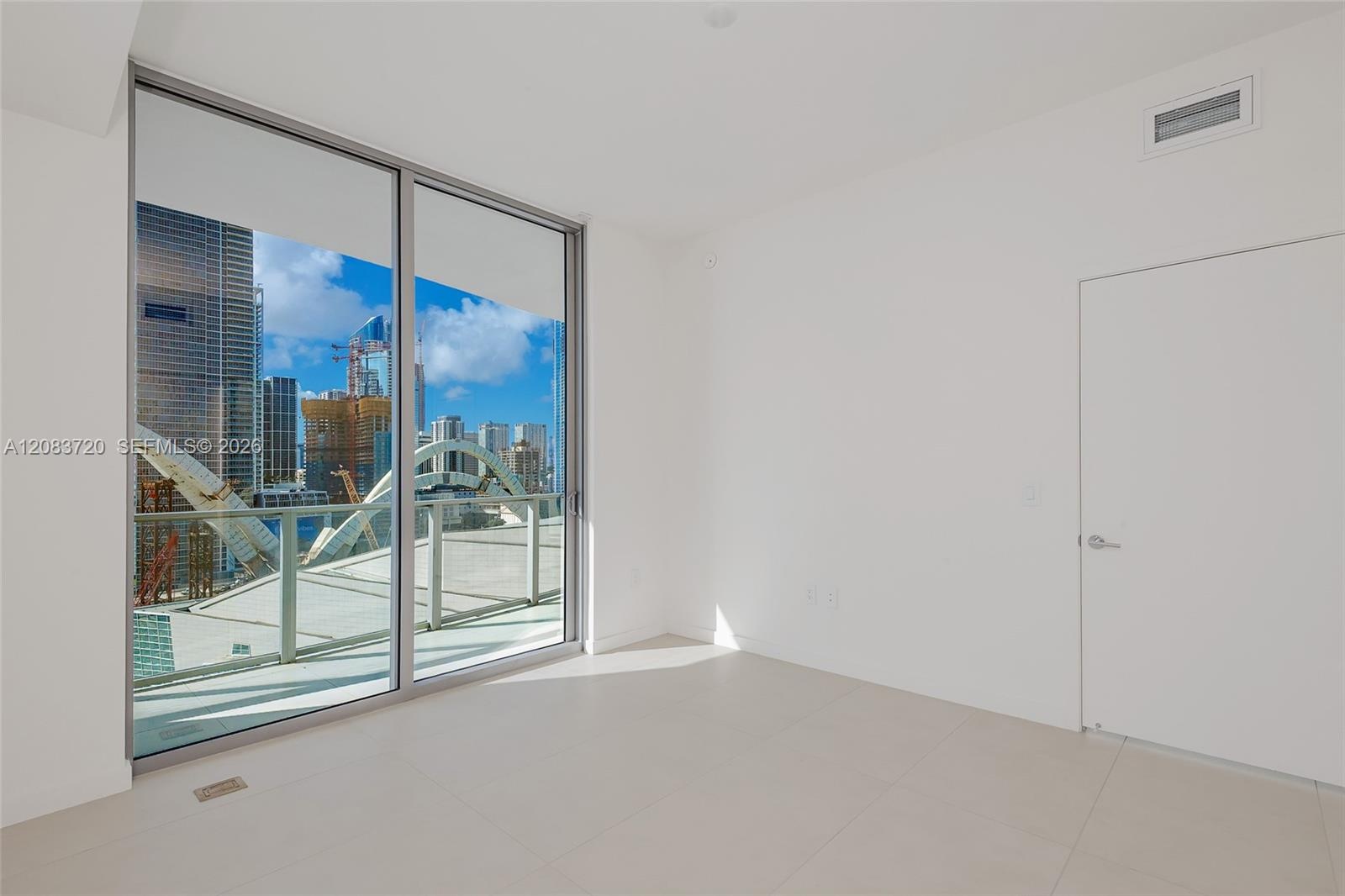 Floor-to-ceiling glass sliding doors, private balcony with metal railing, and light-toned tile flooring