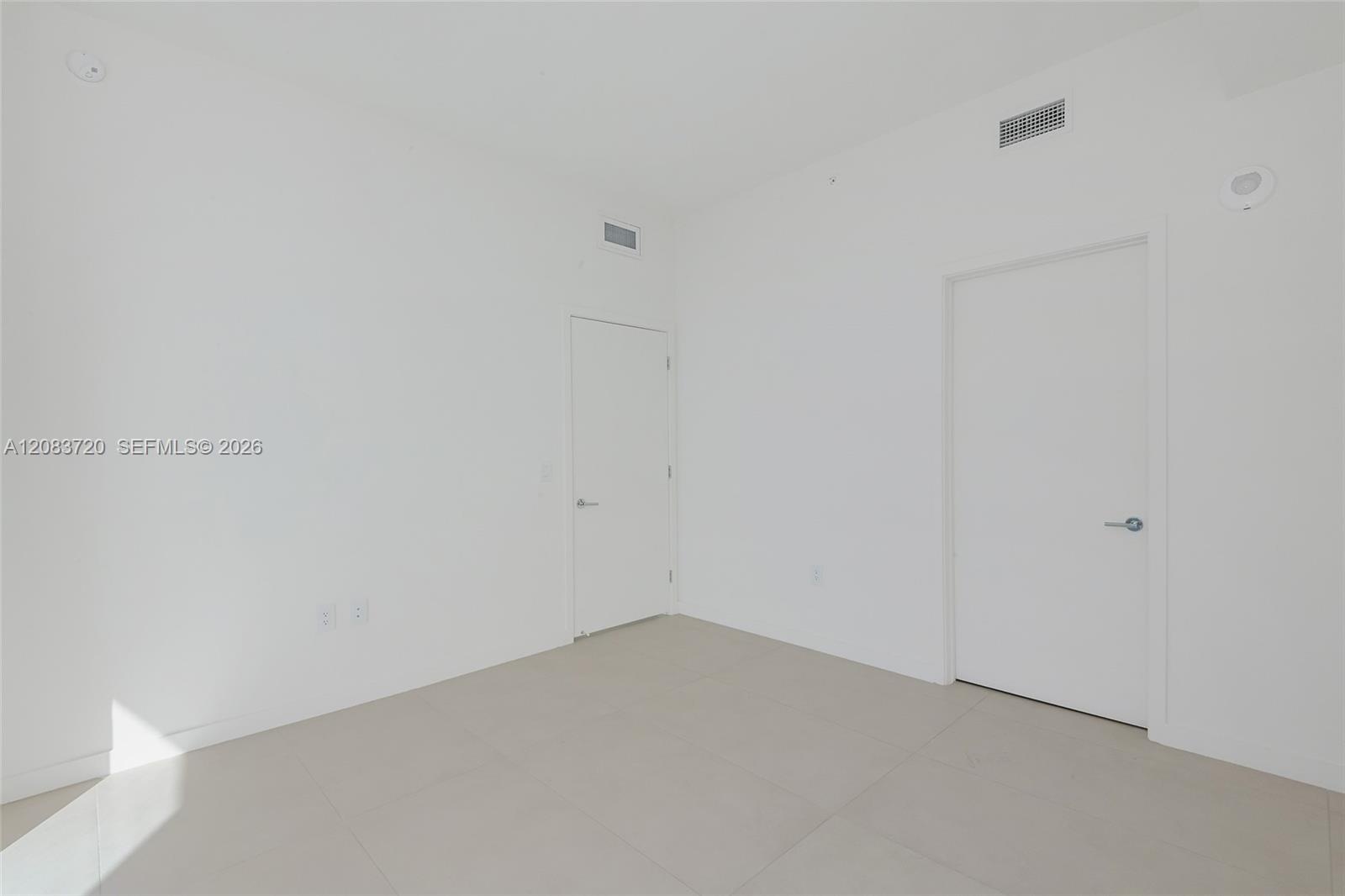 Interior space featuring large-format neutral floor tile, smooth-finish walls, and high-profile interior doors with brushed metal hardware