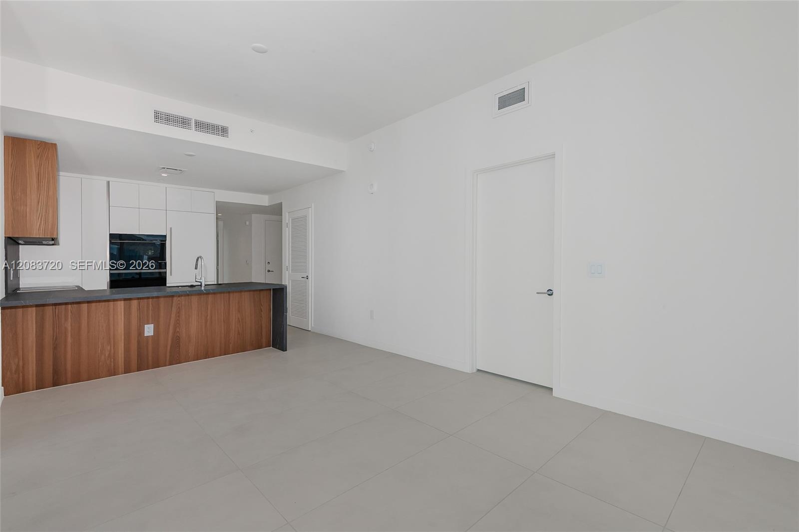 Kitchen featuring wood-finish cabinetry, white matte upper cabinets, dark solid-surface countertops, and large-format tile flooring