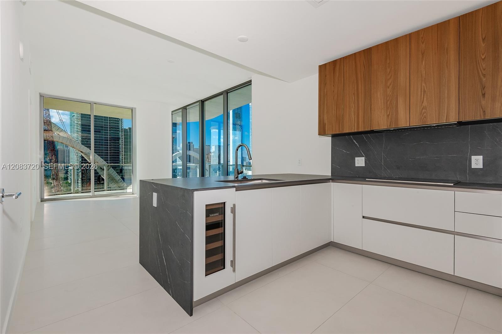 Modern kitchen featuring white flat-panel cabinetry, wood-veneer upper cabinets, integrated wine refrigerator, dark stone-finish countertops and backs