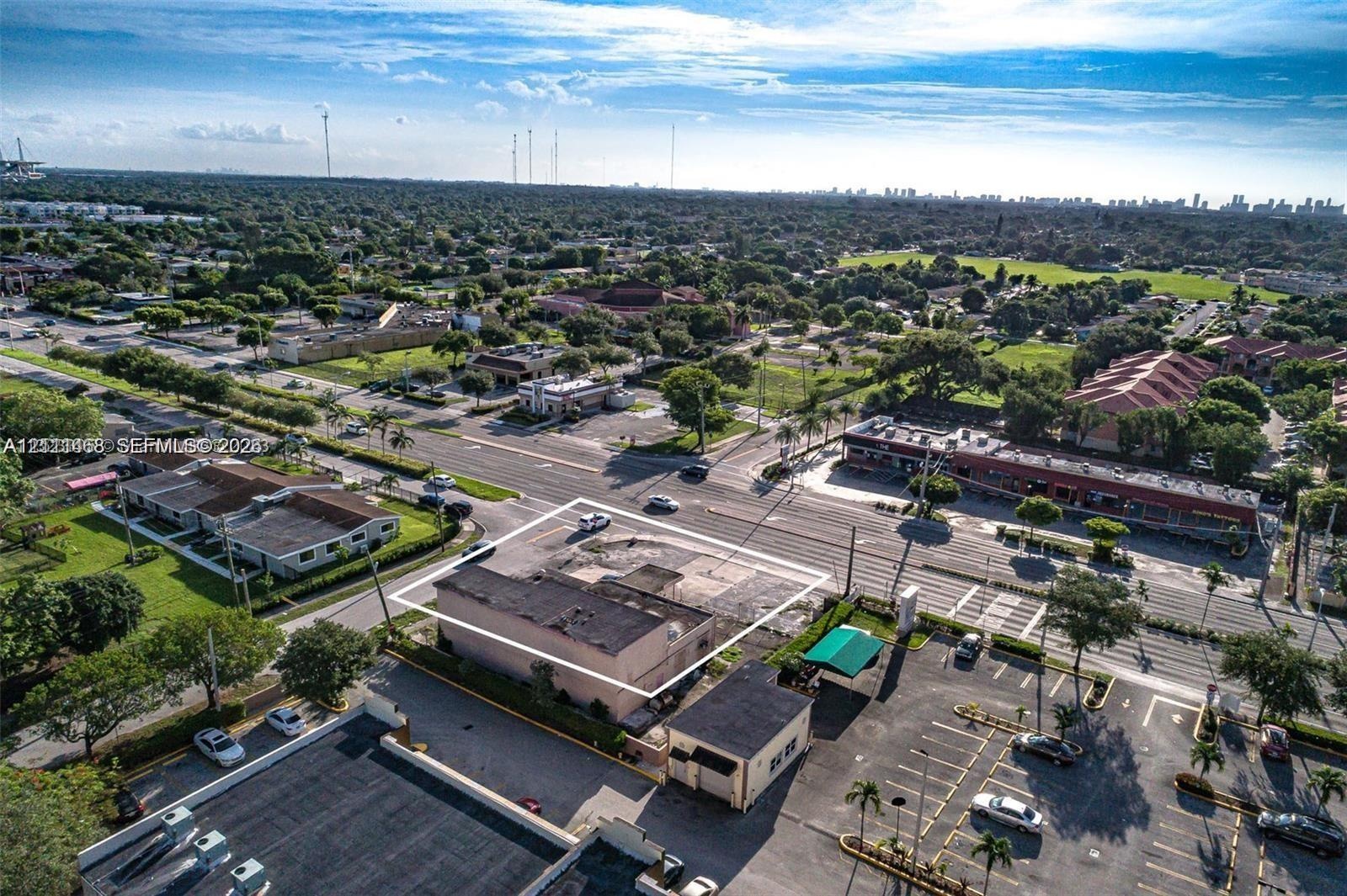 Aerial perspective of a corner commercial property featuring paved surface parking, multi-directional road access, and a flat-roof structure