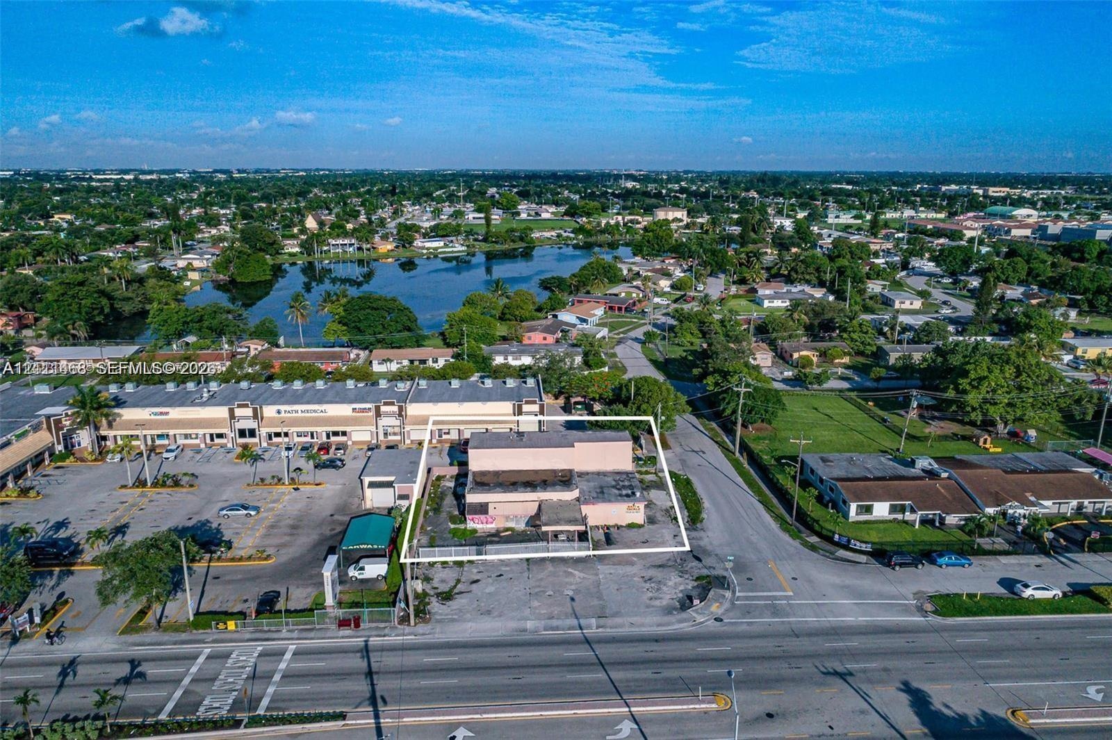 Aerial perspective of a corner commercial property featuring direct street access, a paved parking lot, and proximity to a regional waterway
