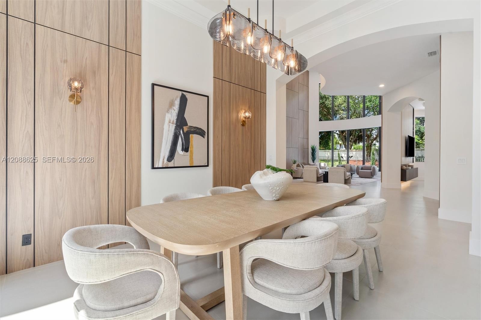 Dining space featuring wood-paneled accent walls, integrated wall-mounted lighting, a multi-pendant glass chandelier, and soaring arched architectural