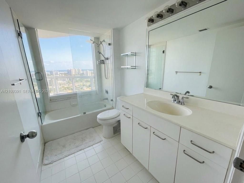 Bathroom featuring a white vanity with integrated countertop sink, full-width wall mirror, shower-tub combination with glass enclosure, and large-form